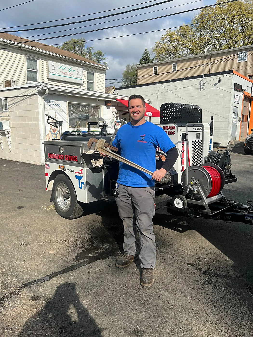 Owner of Sabra Drain & Sewer with a pipe wrench beside the hydro-jetting trailer